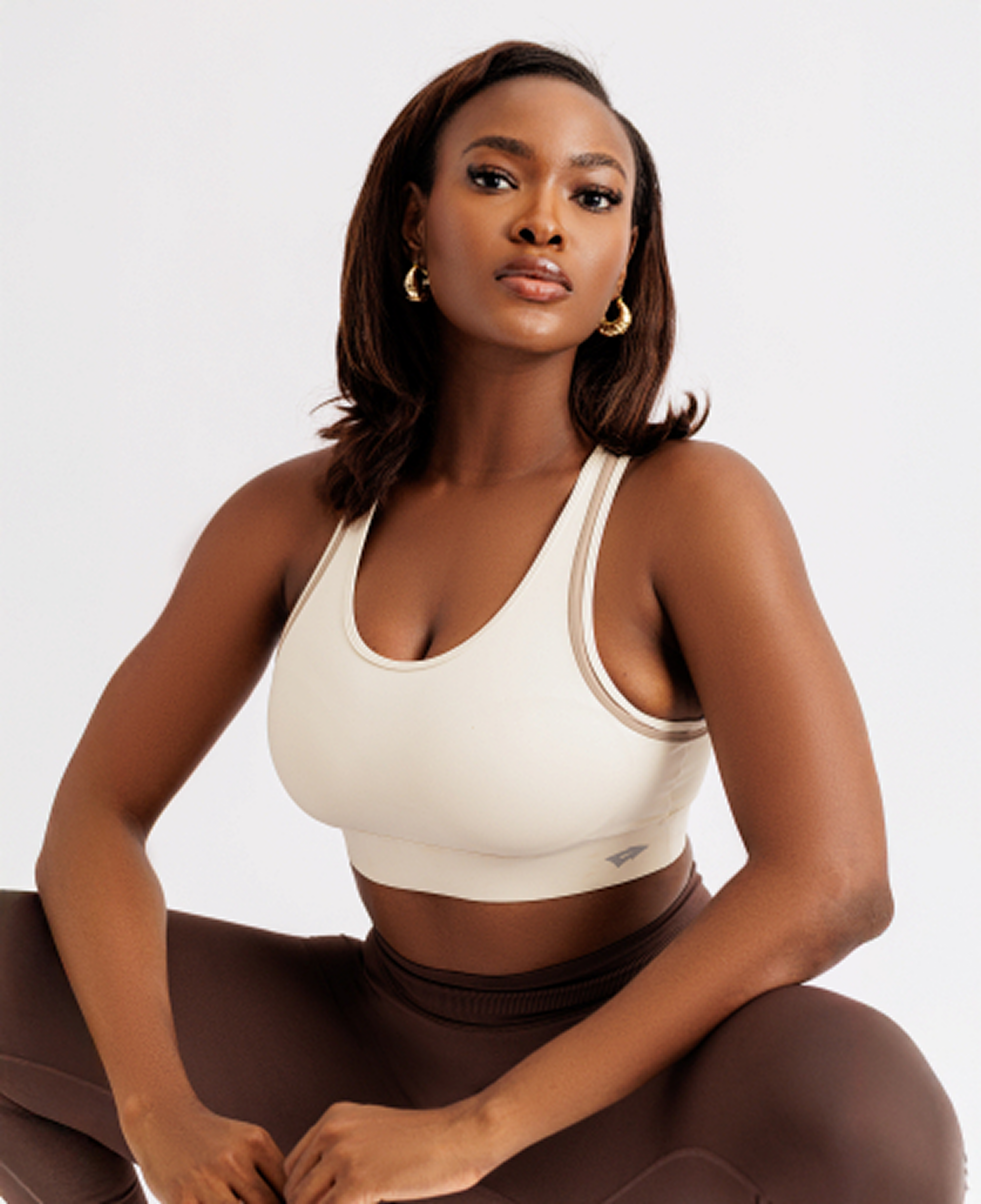 Woman wearing a beige sports bra and brown leggings on a white background